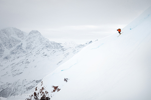 a young man quickly skis down a snow-covered glacier against the backdrop of high mountains