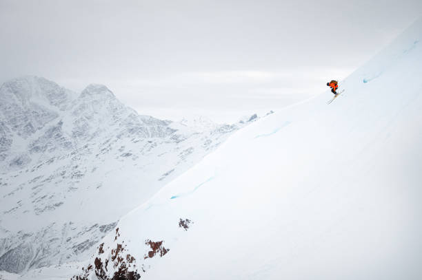 um jovem rapidamente esquia por uma geleira coberta de neve contra o pano de fundo de montanhas altas - freeride - fotografias e filmes do acervo