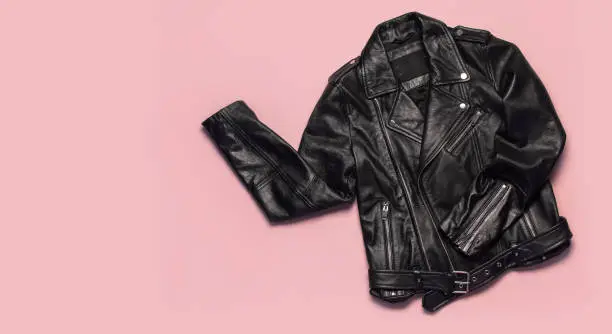 Photo of Black women's leather jacket on pink background top view. Fashionable modern trendy women's clothing. Vintage biker jacket. Black genuine leather