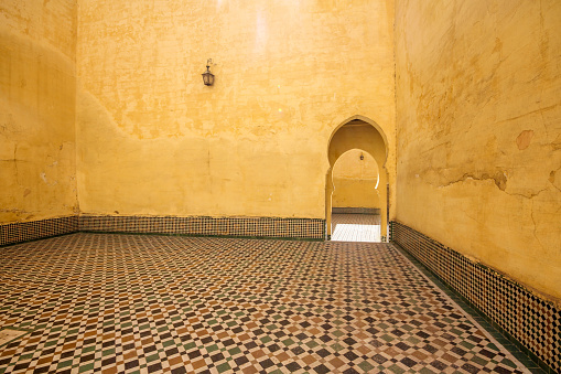 Meknes, Morocco-September 22, 2013: An arched door and yellow walls in the courtyard of Moulay Ismail Tomb. The floors are ceramic tiled.