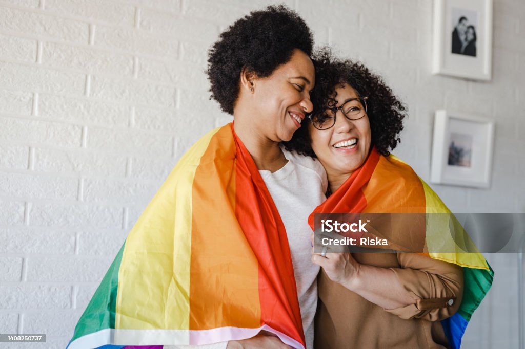 LGBTQIA Pride event. Equality. Portrait of a lesbian couple embracing and wearing rainbow flag. Love and human rights. African-American Ethnicity Stock Photo
