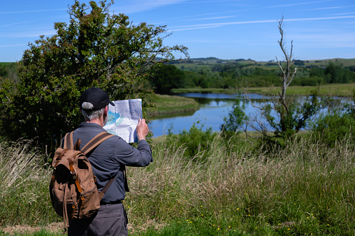 Mature man standing in a rural scene next to a river checking his location on a map