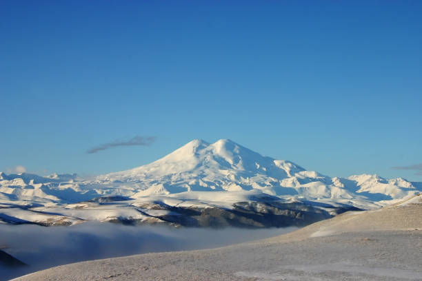 Elbrus is a high mountain. Dormant volcano. mountain covered with snow on blue sky background. Caucasus mountains. Fog and slopes stock photo