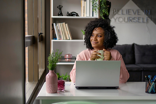 African American woman  drinking tea while working on laptop