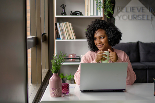 African American woman  drinking tea while working on laptop