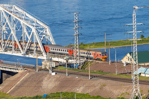 Passenger electrical train moving on railway bridge Yenisey river in Krasnoyarsk, Russia. Commuter passenger train passing on metal railroad bridge