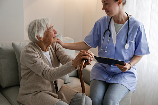 Hospital nurse with a stethoscope, holding a clipboard with medical history for an elderly lady. Senior woman and her designated care giver discussing test results. Background, close up, copy space.