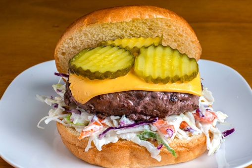 cheese burger resting on cole slaw and top with pickles on a brioche bun