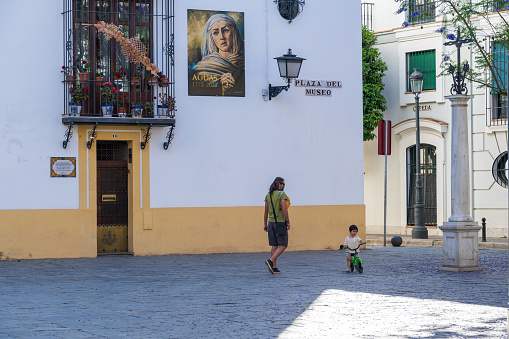 Seville, Spain -- May 16, 2022. Photo of a child riding a small bike in Plaza Del Museo while the father watches.