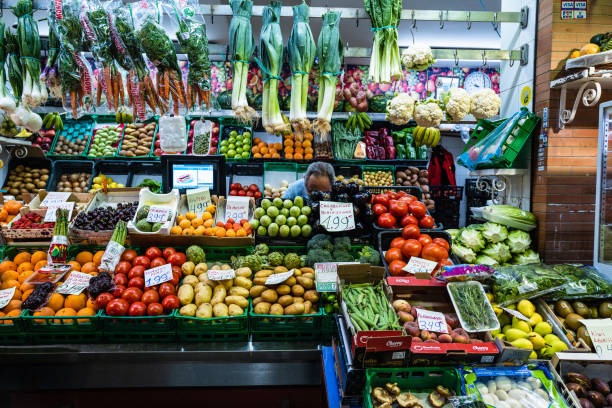 Triana, Seville, Spain — May 27, 2022. In this photo, a grocer is almost hidden among the fruits and vegetables that are for sale.