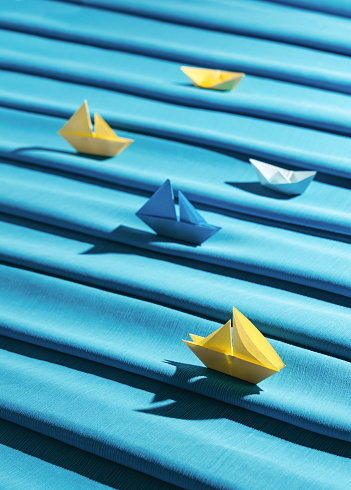 Summer sea travel concept with paper origami sail boats and blue fabric as waves.