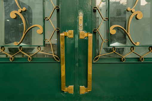 Old green iron door with big handles, bars and golden locks.