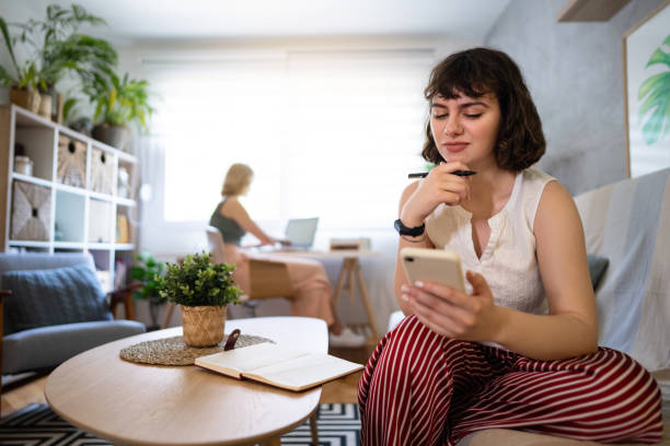 istock Woman using mobile phone while her female roommate working on laptop 1408269130