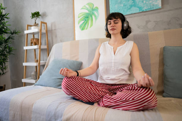 音楽を聴きながら蓮の姿勢で瞑想する若い白人女性 - lotus position audio ストックフォトと画像