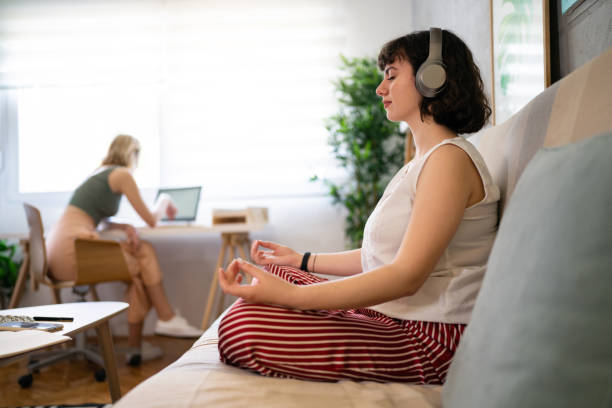 istock Woman meditating in lotus position while her roommate working on laptop 1408269885