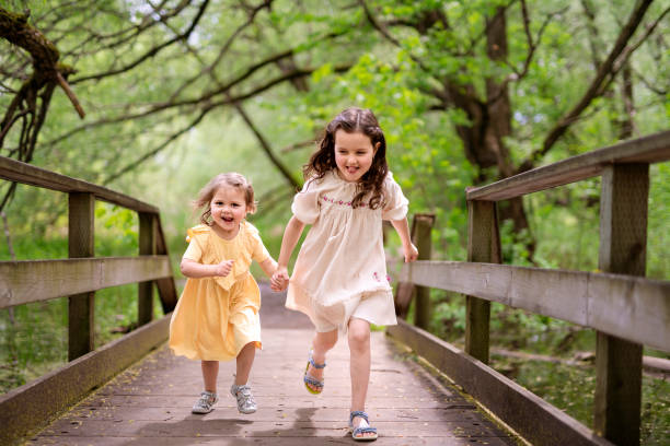 A Two cute sisters girls run outside in forest