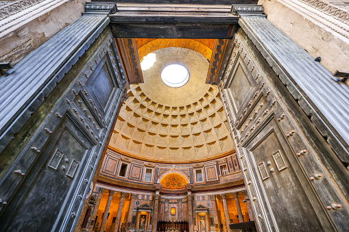 A suggestive wide view of the majestic Roman Pantheon, in the heart of Ancient Rome, through the main door of the temple. In the background below the central apse with the main altar. Built in 27 BC by the Consul Marco Vispanio Agrippa for the Emperor Augustus and dedicated to all the Roman divinities, the majestic Pantheon is one of the best preserved Roman structures in the Eternal City and in the world. In addition, the Pantheon is also a Catholic church consecrated in 609 AD by Pope Bonficio IV and called the Basilica of Santa Maria ad Martyres. Within its perimeter some members of the Italian royal family and famous artists are buried, including the painter Raphael, a great protagonist of Renaissance art. The dome of the Pantheon, built in concrete and brick, is a masterpiece of engineering and the prototype of all the domes subsequently built in Christian churches in Europe. With a diameter of 43.44 meters, it is still the largest dome in the world today. In 1980 the historic center of Rome was declared a World Heritage Site by Unesco. Super wide angle image in High Definition format.