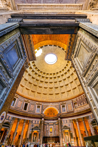 A suggestive wide view of the majestic Roman Pantheon, in the heart of Ancient Rome, through the main door of the temple. In the background below the central apse with the main altar. Built in 27 BC by the Consul Marco Vispanio Agrippa for the Emperor Augustus and dedicated to all the Roman divinities, the majestic Pantheon is one of the best preserved Roman structures in the Eternal City and in the world. In addition, the Pantheon is also a Catholic church consecrated in 609 AD by Pope Bonficio IV and called the Basilica of Santa Maria ad Martyres. Within its perimeter some members of the Italian royal family and famous artists are buried, including the painter Raphael, a great protagonist of Renaissance art. The dome of the Pantheon, built in concrete and brick, is a masterpiece of engineering and the prototype of all the domes subsequently built in Christian churches in Europe. With a diameter of 43.44 meters, it is still the largest dome in the world today. In 1980 the historic center of Rome was declared a World Heritage Site by Unesco. Super wide angle image in High Definition format.