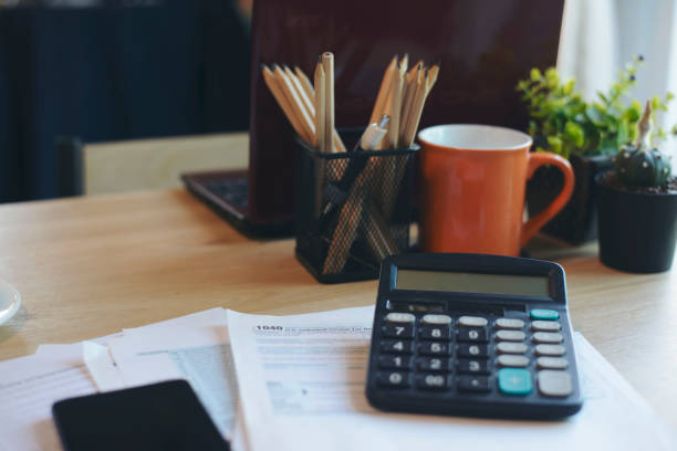istock Home Office Desk Concept.Laptop, summary report, chart, and calculator for accountant or bookkeeper plan annual budget and tax. Computer, calculator, and pencil placed on wooden table, working at home 1408271915