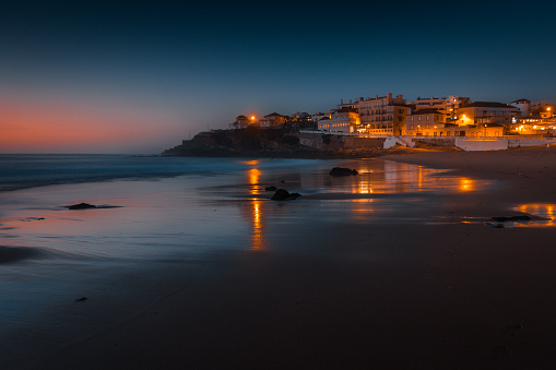 Amazing landscape of the Atlantic ocean coast at sunset. View of colorful dramatic sky and buildings near a sandy beach. Long exposure image. Beach of Praia das Macas. Portugal.