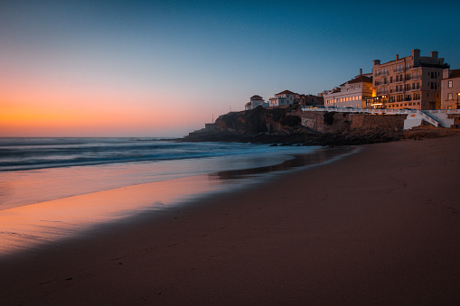 Amazing landscape of the Atlantic ocean coast at sunset. View of colorful dramatic sky and buildings near a sandy beach. Long exposure image. Beach of Praia das Macas. Portugal.