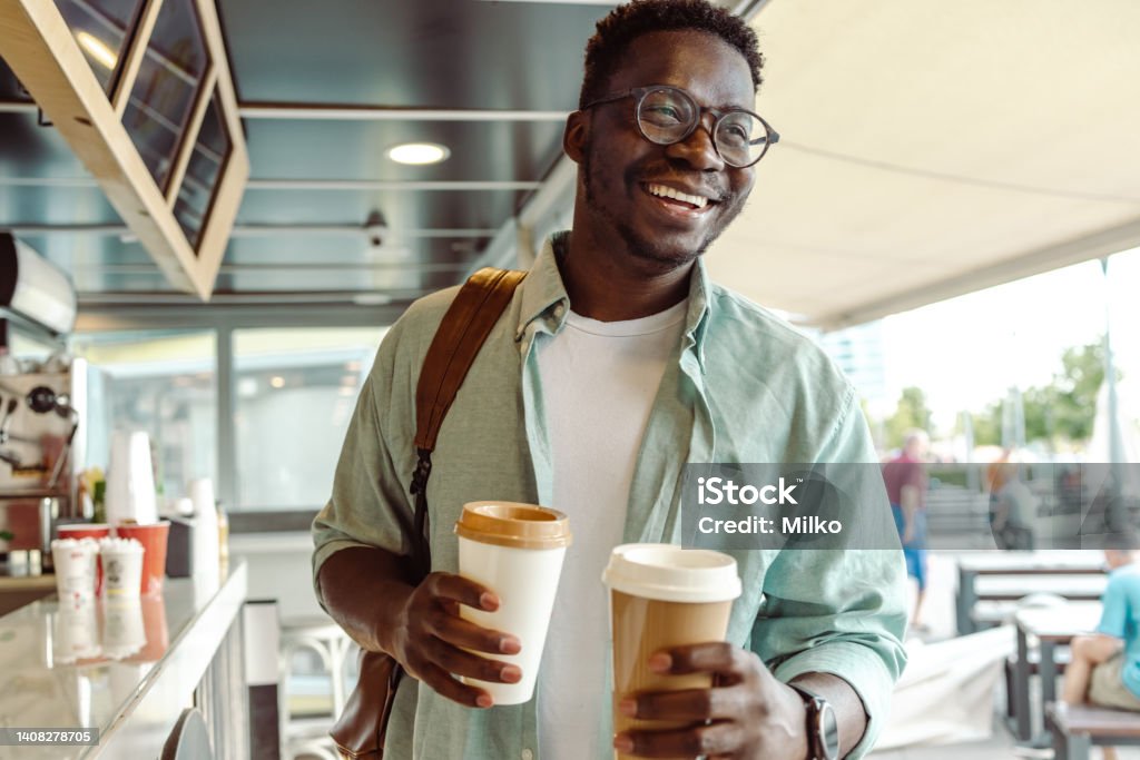 African-American student picking up a coffee Portrait of a happy African American man holding two cups of coffee Coffee - Drink Stock Photo