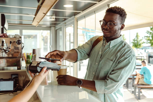 un joven afroamericano pagando en la cafetería - pago por movil fotografías e imágenes de stock
