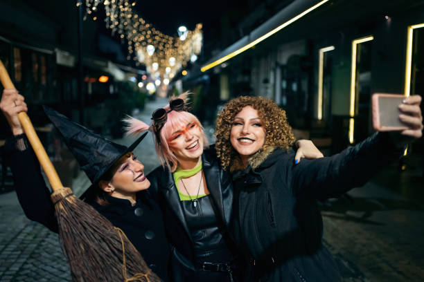 Three young women in Haloween costumes making selfies on the city street stock photo