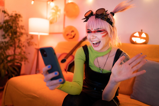 Young Caucasian woman in steampunk costume having a video call over phone at the Halloween party.
