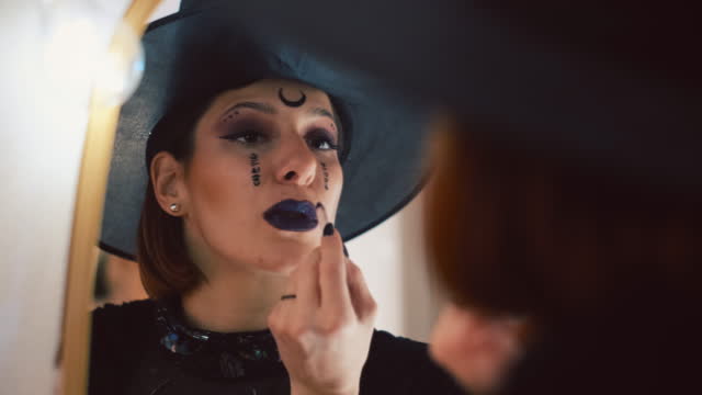 Young Caucasian woman in witch costume doing make-up for Halloween party