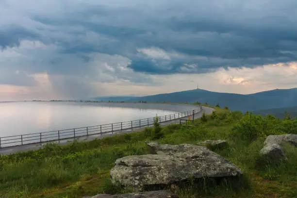Upper water reservoir of the pumped storage hydro power plant Dlouhe Strane in Jeseniky Mountains, Czech Republic. Top of the Praded mountain behind the lake. Summer rainy morning, sunrise, storm clouds.