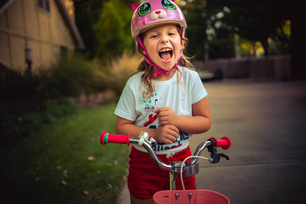Young girl in bicycle helmet celebrates after learning how to ride her bicycle