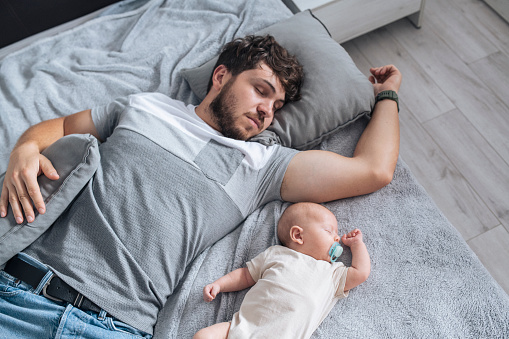 Young father and baby boy sleeping on bed at home.
