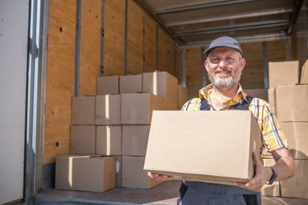 ein fröhlicher arbeiter entlädt kartons mit waren - delivering freedom shipping truck stock-fotos und bilder