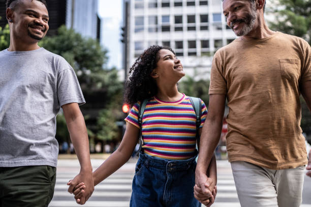 счастливая и гордая девушка переходит улицу со своими двумя отцами - adoption early teens teenager family стоковые фото и изображения
