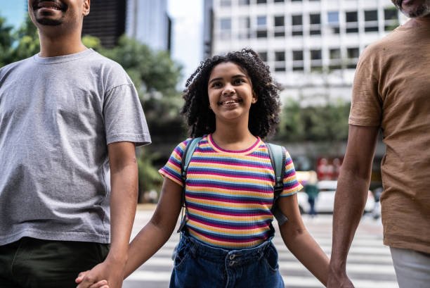 garota feliz e orgulhosa atravessando a rua com seus dois pais - adoption early teens teenager family - fotografias e filmes do acervo