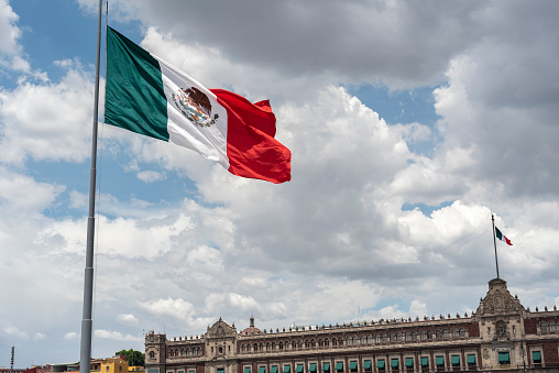 Mexican flag waving with blue sky and clouds and the national palace in the background in Mexico City, Mexico Flag.