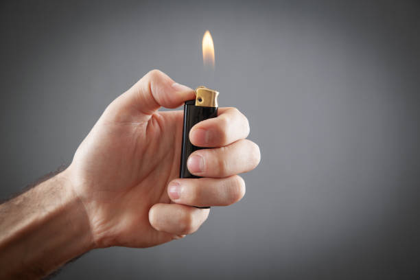 Male hand burning lighter in grey background. Male hand burning lighter in grey background. cigarette lighter stock pictures, royalty-free photos & images