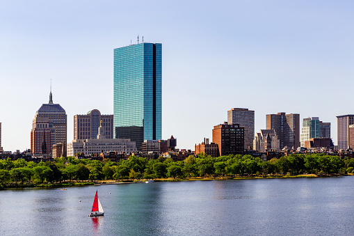 Boston, Massachusetts, USA - July 10, 2022: Boston's Back Bay neighborhood viewed across the Charles River. Hancock Tower skyscraper and sailboat sailing on the river.