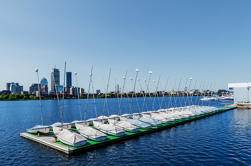 Boston, Massachusetts, USA - July 10, 2022: Rows of covered sailboats on a dock on the Charles River. Boston's Back Bay neighborhood seen across the river.