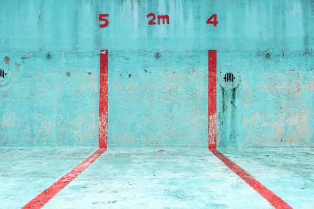 Photo of Focus on a piece of an abandoned swimming pool in a bright blue colour with red stripes. The lanes and depth are indicated.