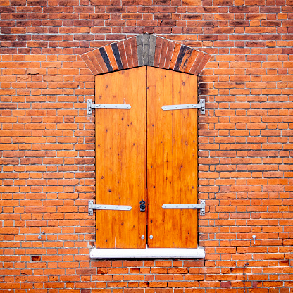 Wooden shutters on a window in the red brick wall of an old industrial building.