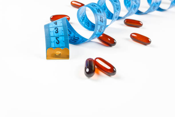 Pile of leptin capsules with blue measuring tape on white background. Concept of losing weight, diet, fat burning, healthy eating. Pile of leptin capsules with blue measuring tape on white background. Concept of losing weight, diet, fat burning, healthy eating. Copy space. diet pills stock pictures, royalty-free photos & images