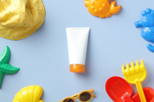 Flat lay sunscreen lotion tube, kids sunglasses and sand molds on blue table. Baby skin care, sun protection concept.