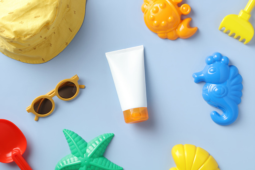 Flat lay sunscreen lotion tube, kids sunglasses and sand molds on blue table. Baby skin care, sun protection concept.