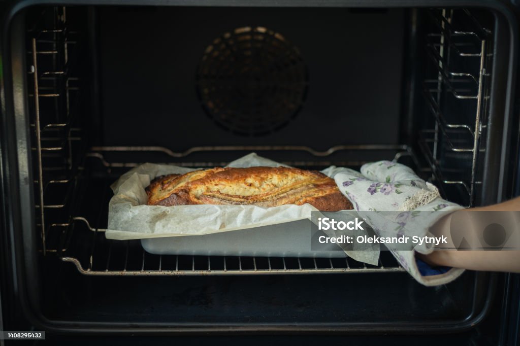 Woman wearing potholder taking fresh banana bread out of the oven. Close up of hot homemade pastry Baking Bread Stock Photo