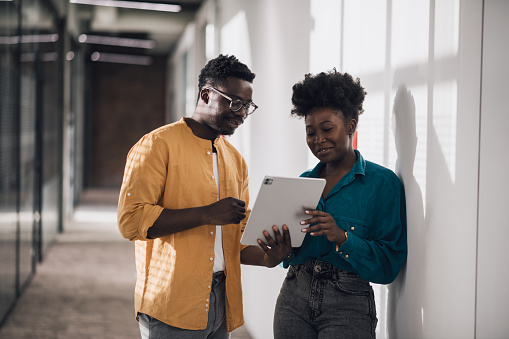 Happy and smiling young black businesspeople. Attractive young African-American woman and man at work. Young students working on a digital tablet in their office building.