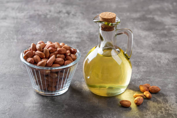 peanut oil in a glass jug and raw peeled groundnut in a glass bowl over gray background. arachis hypogaea as edible seeds and oil crop. monounsaturated cooking oil. vegetarian snack. - arachis hypogaea fotos imagens e fotografias de stock