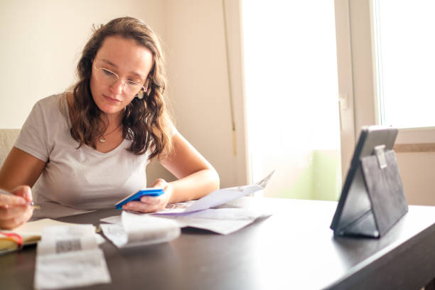 istock Woman checking her bills at her dining table and doing math with calculator consulting a financial assistant by computer 1408298067