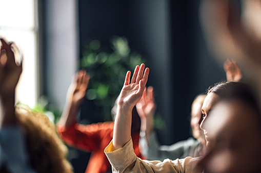 Group of people sitting on a seminar. They have their hand raised.